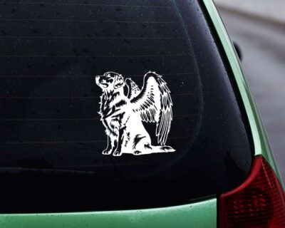 Vinyl decal of a majestic golden retriever dog with large angel wings. The dog is depicted sitting upright with a calm and serene expression, its head slightly tilted upward as if looking toward the heavens. Detailed fur markings create a textured, realistic look throughout the body, while the strong wings extend gracefully from its back, showcasing layered feathers with intricate line work.