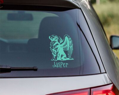 Vinyl decal of a majestic golden retriever dog with large angel wings. The dog is depicted sitting upright with a calm and serene expression, its head slightly tilted upward as if looking toward the heavens. Detailed fur markings create a textured, realistic look throughout the body, while the strong wings extend gracefully from its back, showcasing layered feathers with intricate line work.